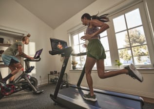One person runs on the Peloton Tread at home and another cycles on a Peloton Bike 