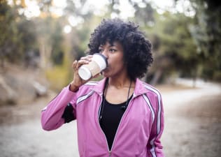 A young woman going for a walk outdoors in workout gear while drinking coffee before a workout.