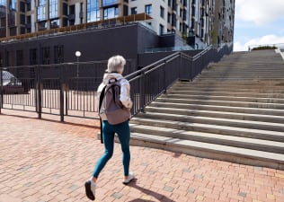 Woman wearing a backpack walks towards steps outside
