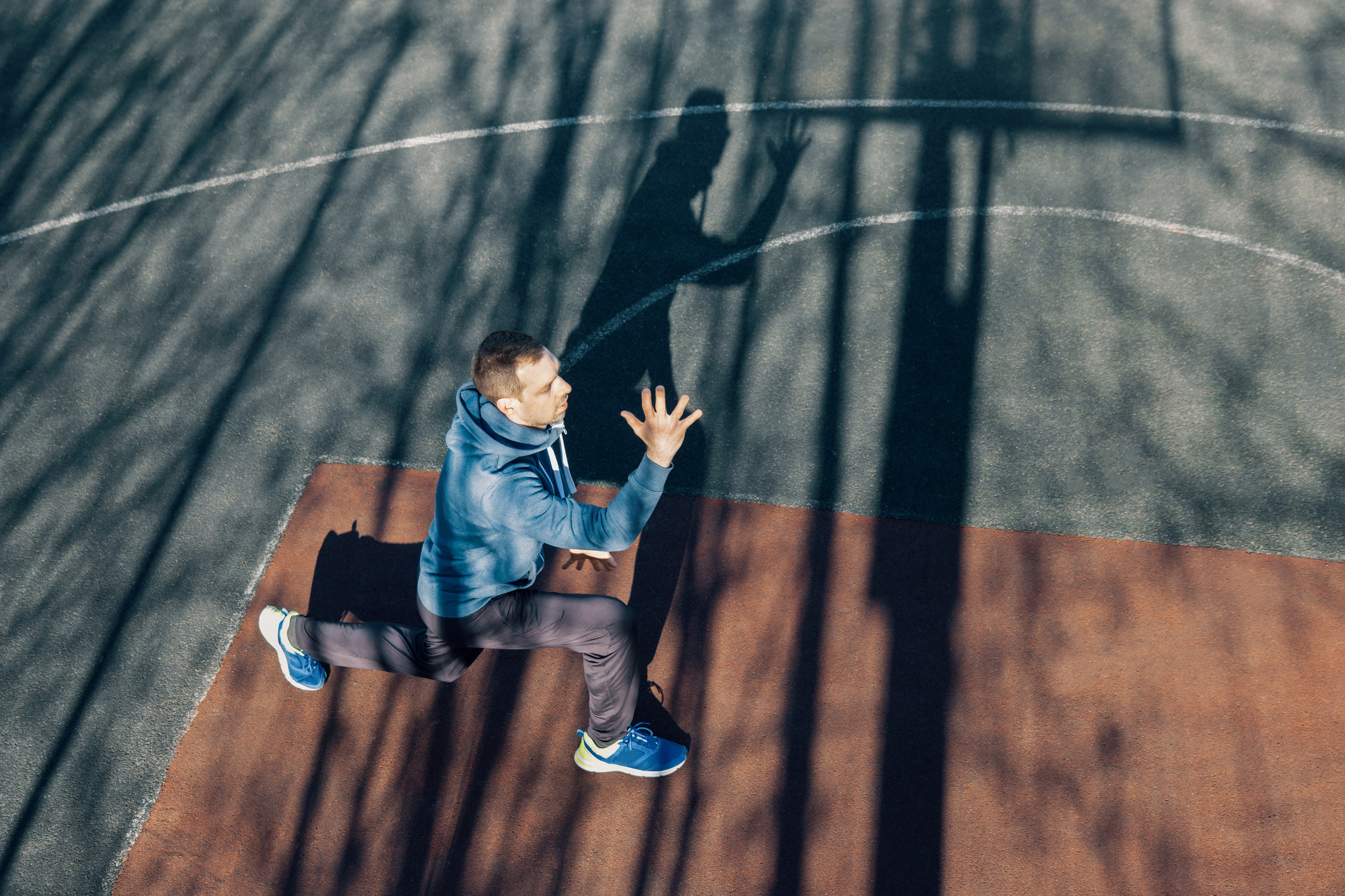 Man does a lunge exercise on a basketball court outdoors