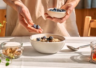 High-Fiber Foods: A person adding blueberries to a bowl of oatmeal.