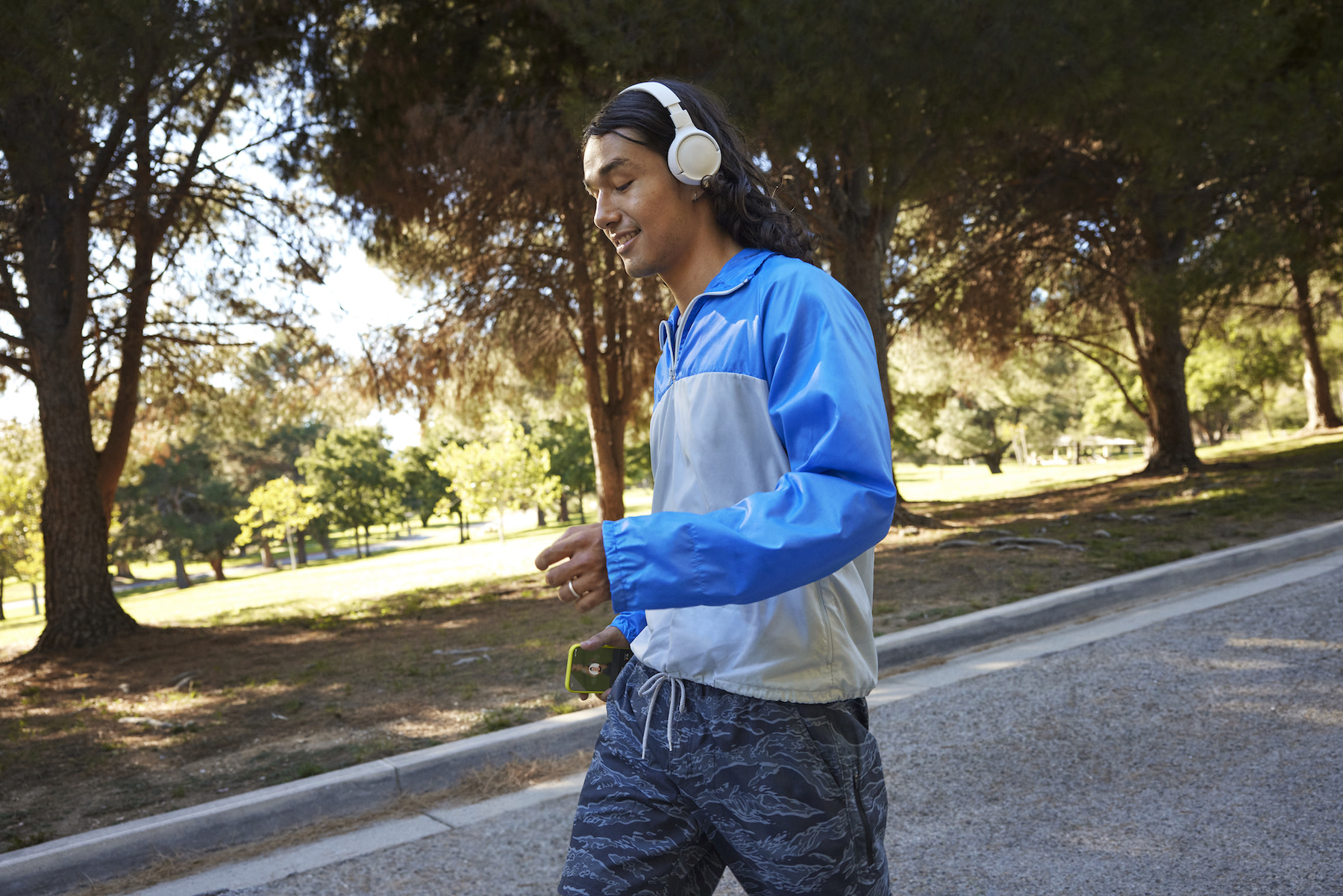 A man walking outside with headphones while holding his phone. Learn how exercise can relieve stress in this article.