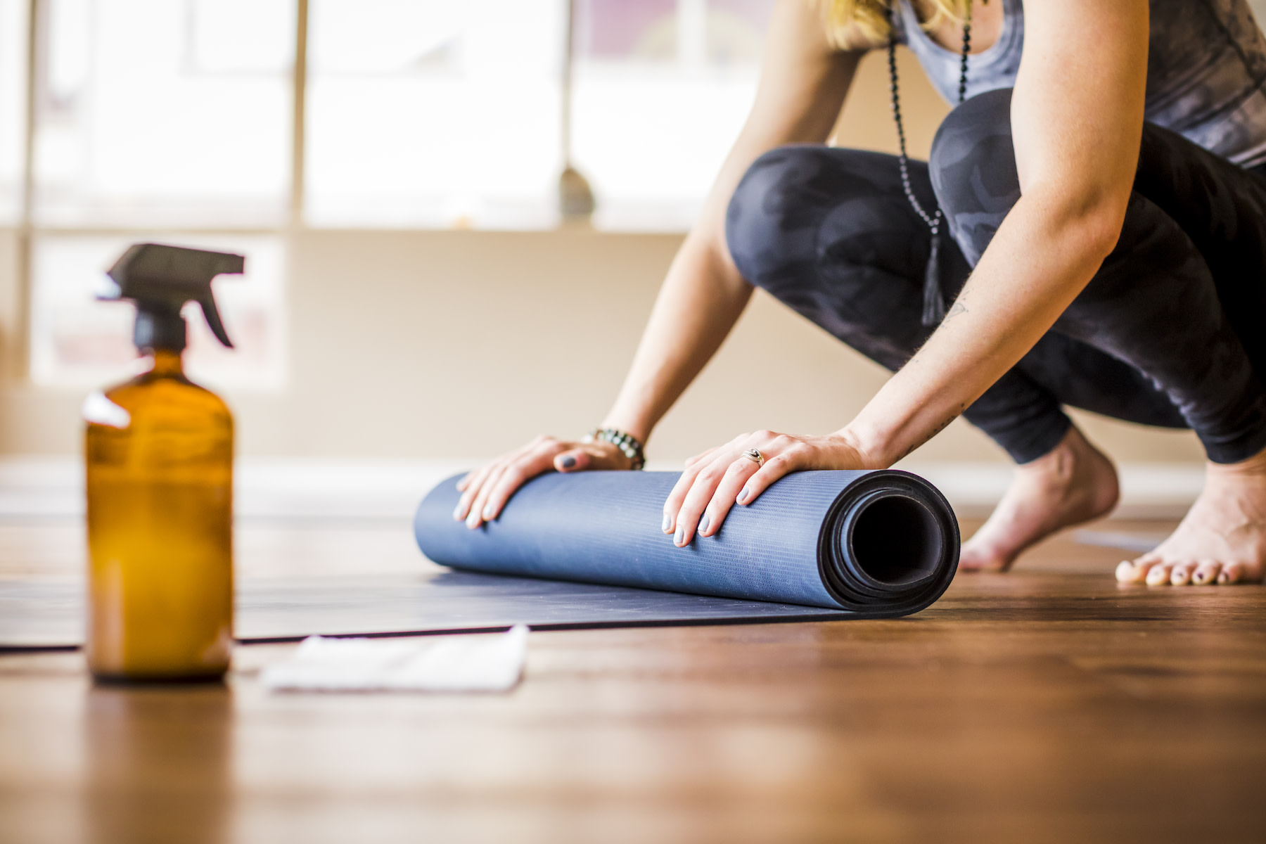 A woman cleaning her yoga mat and rolling it up.