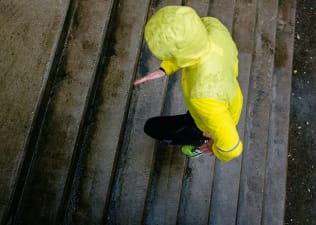 A person in a yellow rain jacket and black pants running in the rain up some stairs.