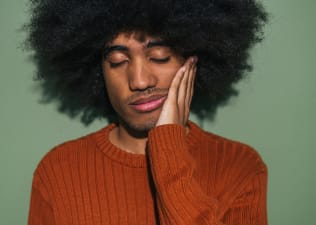 In this image for an article about feeling sleepy after eating, a man is closing his eyes and putting a hand on his cheek in tiredness.
