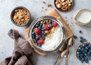 A bowl of yogurt, berries, and granola with an aesthetically pleasing table setting. Yogurt and berries are great foods for gut health. Learn more about what gut health is in this article.
