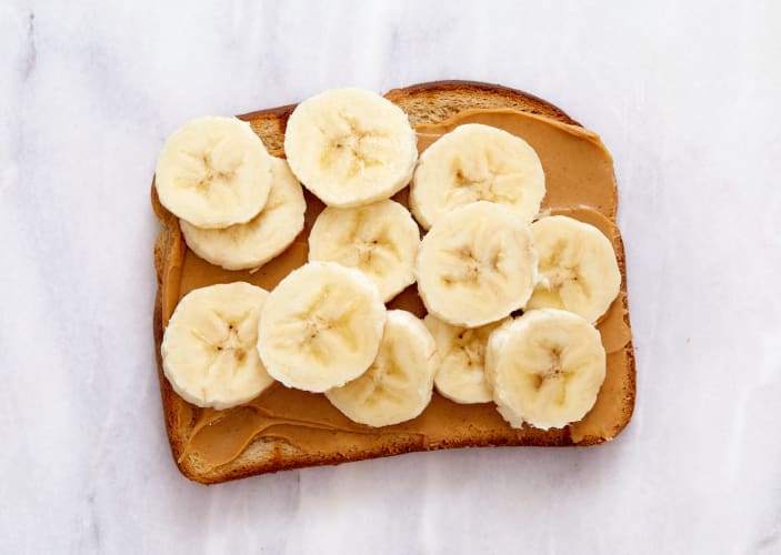 Peanut butter and banana toast, pictured here on a white marble countertop, is a great food to eat before a workout.